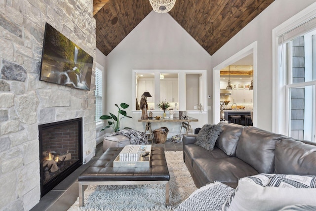 living room with plenty of natural light, a stone fireplace, wooden ceiling, and high vaulted ceiling