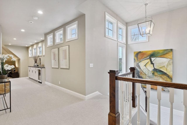 hallway with carpet flooring, beverage cooler, a wealth of natural light, and an inviting chandelier