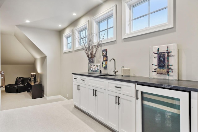 bar with light colored carpet, white cabinetry, beverage cooler, and sink