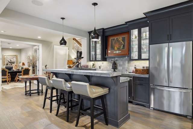 bar featuring tasteful backsplash, pendant lighting, stone countertops, light hardwood / wood-style flooring, and stainless steel refrigerator