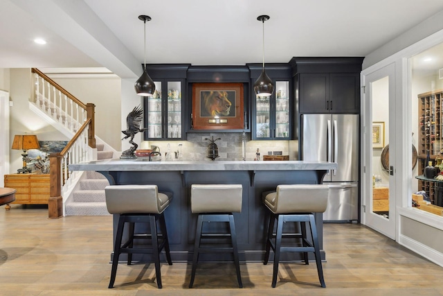 bar featuring decorative light fixtures, stainless steel fridge, and light hardwood / wood-style floors