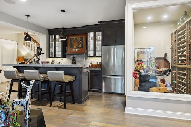 bar with stainless steel fridge, light wood-type flooring, decorative light fixtures, and backsplash