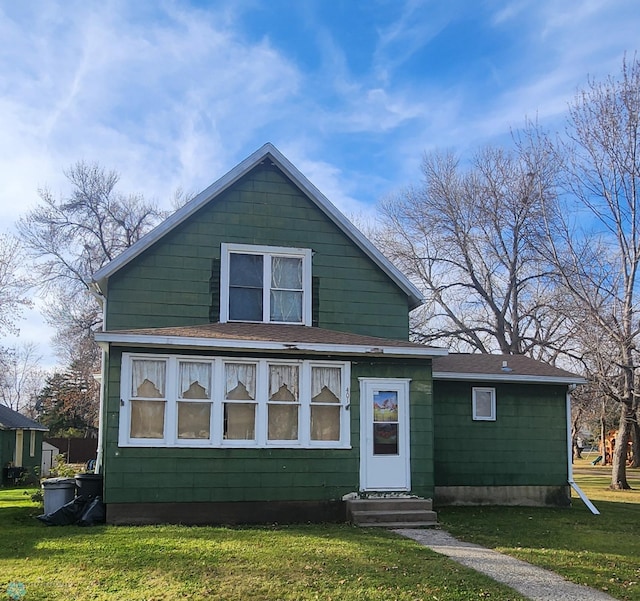 bungalow with entry steps, roof with shingles, and a front lawn