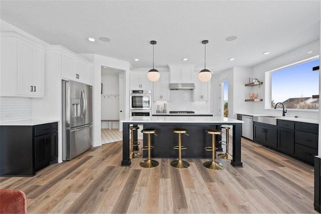 kitchen with white cabinetry, appliances with stainless steel finishes, light hardwood / wood-style floors, and hanging light fixtures