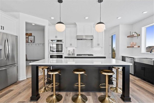 kitchen with white cabinetry, appliances with stainless steel finishes, decorative light fixtures, and light hardwood / wood-style flooring