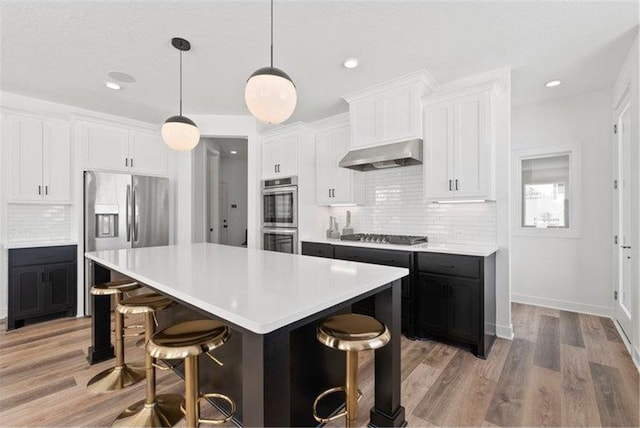 kitchen featuring white cabinetry, appliances with stainless steel finishes, a breakfast bar area, ventilation hood, and a kitchen island