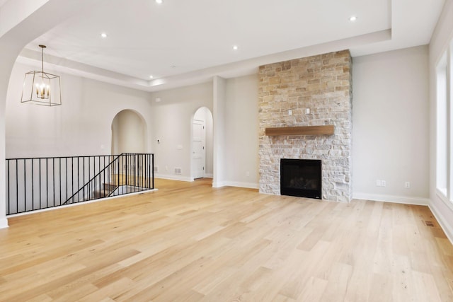 unfurnished living room featuring a chandelier, a raised ceiling, light hardwood / wood-style floors, and a stone fireplace