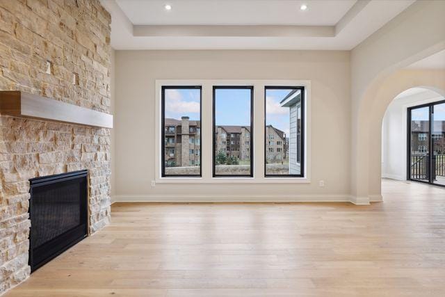 unfurnished living room featuring a raised ceiling, a stone fireplace, and light wood-type flooring