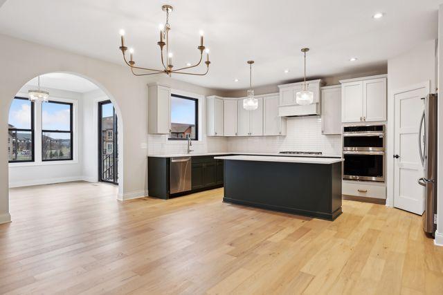 kitchen featuring hanging light fixtures, light wood-type flooring, a kitchen island, white cabinetry, and stainless steel appliances