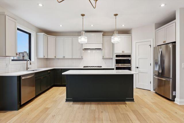 kitchen featuring decorative light fixtures, a kitchen island, light wood-type flooring, and appliances with stainless steel finishes