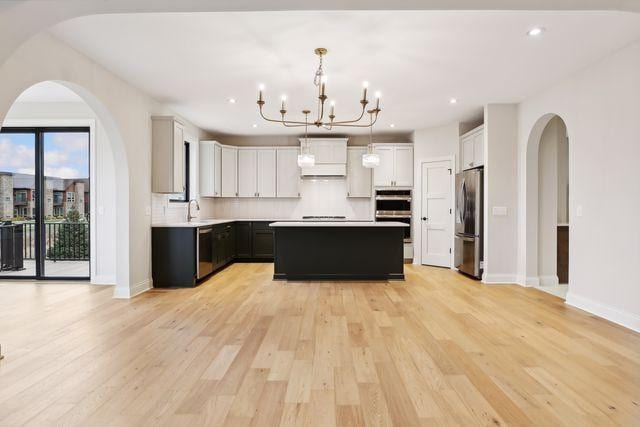 kitchen with stainless steel appliances, decorative light fixtures, a notable chandelier, a center island, and light hardwood / wood-style floors