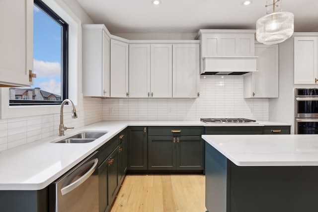 kitchen featuring appliances with stainless steel finishes, premium range hood, sink, pendant lighting, and white cabinetry