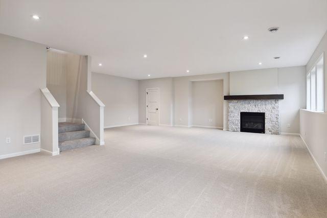 unfurnished living room with light carpet and a stone fireplace