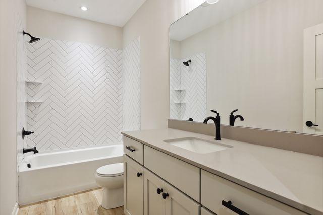 full bathroom featuring hardwood / wood-style flooring, tiled shower / bath combo, toilet, and vanity