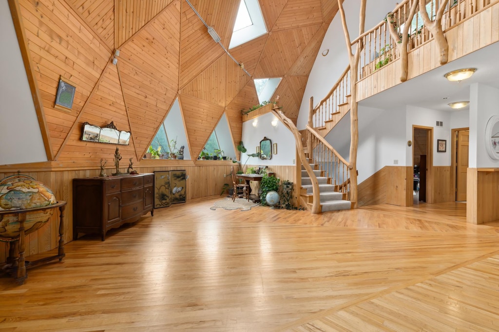 living room with a high ceiling, a skylight, wooden walls, and light hardwood / wood-style floors