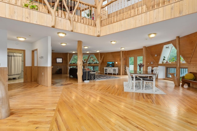 dining space featuring a towering ceiling, a skylight, light hardwood / wood-style flooring, and wood walls