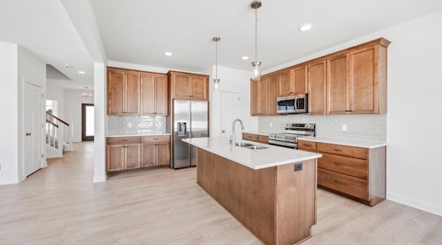 kitchen with a sink, light countertops, appliances with stainless steel finishes, an island with sink, and decorative light fixtures