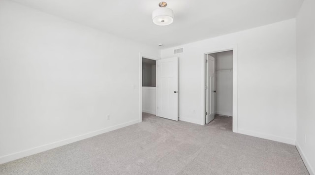 unfurnished bedroom featuring light carpet, baseboards, visible vents, and a walk in closet