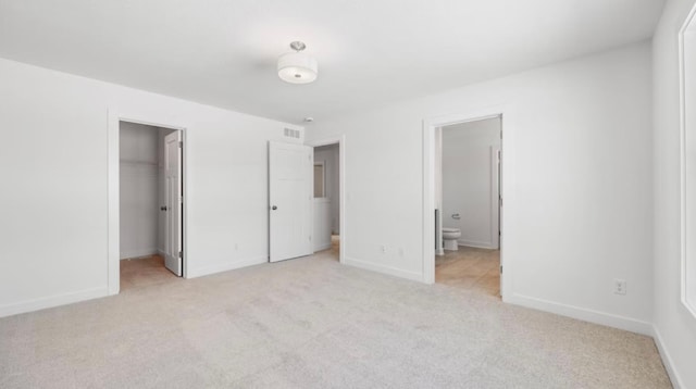 unfurnished bedroom featuring a closet, light colored carpet, a spacious closet, ensuite bath, and baseboards