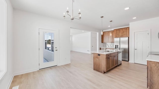 kitchen featuring light countertops, appliances with stainless steel finishes, brown cabinets, an island with sink, and decorative light fixtures