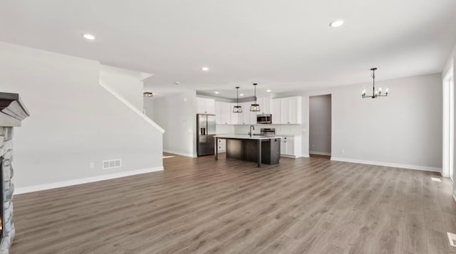 unfurnished living room with a stone fireplace, a notable chandelier, visible vents, baseboards, and light wood-style floors