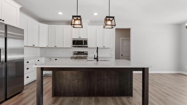 kitchen with stainless steel appliances, light countertops, decorative backsplash, a kitchen island with sink, and a sink