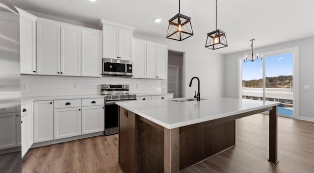 kitchen featuring dark wood-style flooring, a center island with sink, light countertops, appliances with stainless steel finishes, and a sink