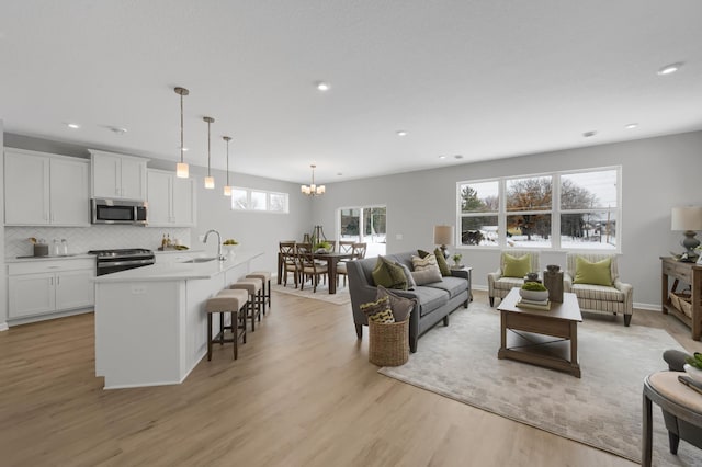 living room featuring an inviting chandelier, sink, a wealth of natural light, and light hardwood / wood-style flooring