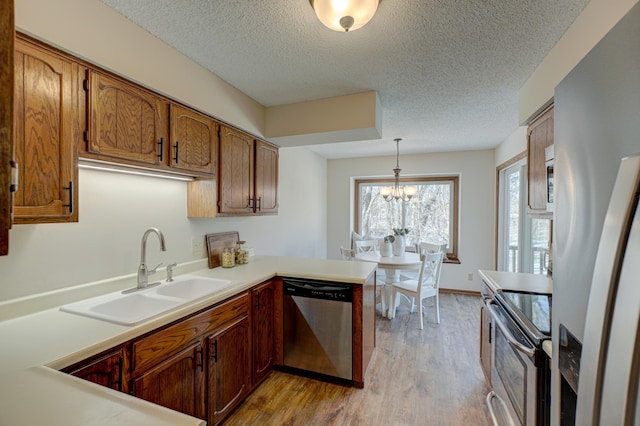 kitchen with sink, hanging light fixtures, appliances with stainless steel finishes, kitchen peninsula, and light hardwood / wood-style floors