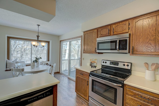 kitchen featuring appliances with stainless steel finishes, hanging light fixtures, a notable chandelier, light hardwood / wood-style floors, and a textured ceiling