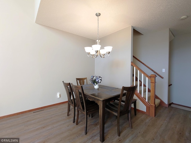 dining area featuring hardwood / wood-style flooring, a notable chandelier, and a textured ceiling