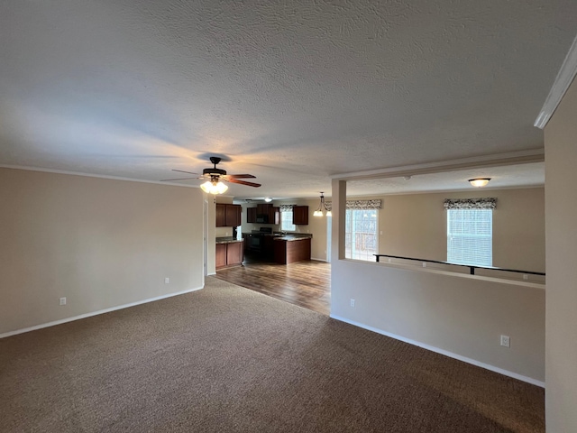 unfurnished living room with a textured ceiling, dark colored carpet, ornamental molding, and ceiling fan with notable chandelier