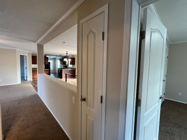 hallway featuring a textured ceiling, ornamental molding, and carpet floors