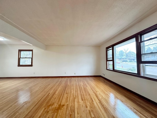 spare room with beam ceiling, light hardwood / wood-style flooring, and a textured ceiling