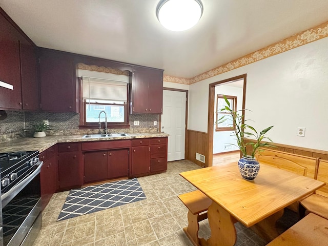 kitchen with wood walls, stainless steel gas range oven, sink, and tasteful backsplash