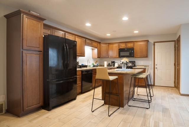 kitchen featuring black appliances, light stone countertops, a breakfast bar area, a center island, and light wood-type flooring