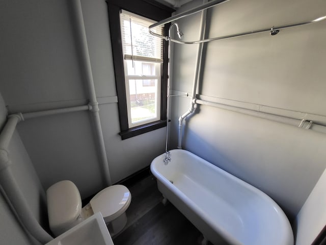 bathroom featuring wood-type flooring, a tub to relax in, and toilet