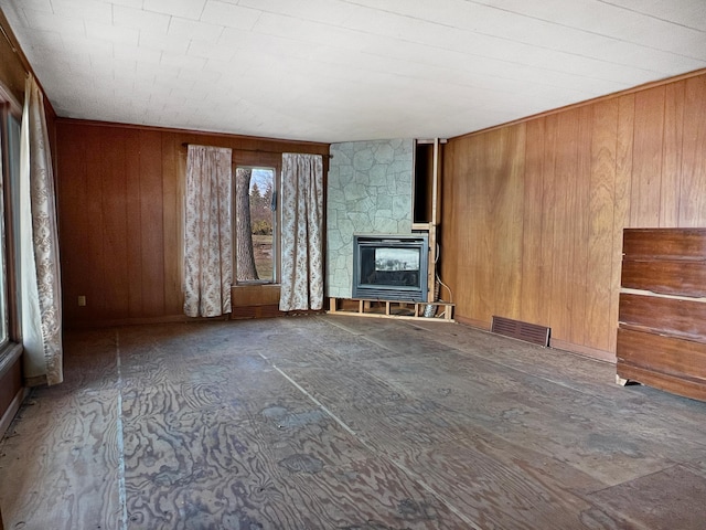 unfurnished living room featuring a stone fireplace and wooden walls