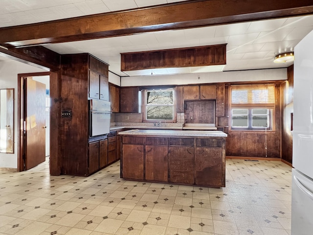 kitchen with white oven, dark brown cabinets, a healthy amount of sunlight, and a center island