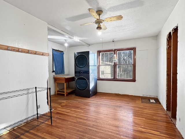 living area featuring a textured ceiling, stacked washer and dryer, hardwood / wood-style floors, and ceiling fan