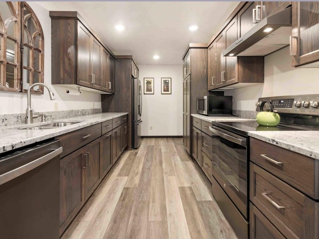 kitchen featuring appliances with stainless steel finishes, light stone counters, dark brown cabinets, sink, and light hardwood / wood-style flooring