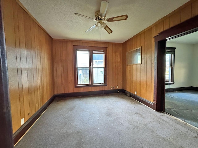 spare room with a textured ceiling, wooden walls, and ceiling fan