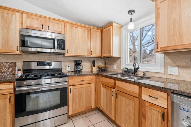 kitchen with lofted ceiling, sink, dark stone countertops, light tile patterned floors, and stainless steel appliances