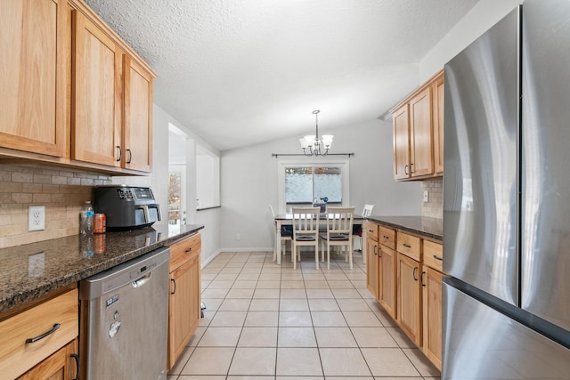 kitchen featuring lofted ceiling, appliances with stainless steel finishes, dark stone countertops, tasteful backsplash, and decorative light fixtures