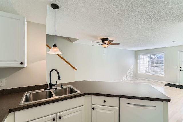 kitchen featuring dark countertops, a textured ceiling, white cabinetry, pendant lighting, and a sink