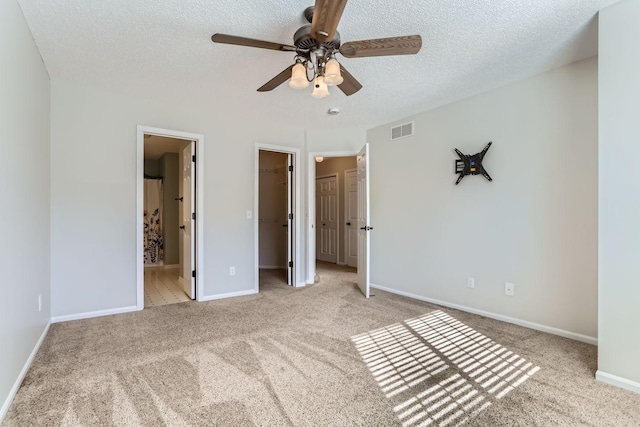 unfurnished bedroom featuring visible vents, ensuite bath, a walk in closet, a textured ceiling, and carpet flooring