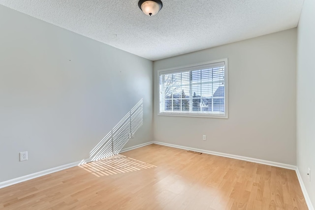 spare room featuring a textured ceiling, baseboards, and wood finished floors