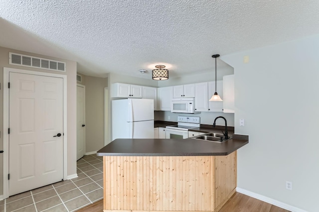 kitchen featuring white appliances, visible vents, dark countertops, a peninsula, and a sink