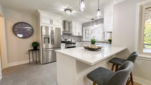 kitchen featuring a kitchen breakfast bar, wall chimney range hood, kitchen peninsula, white cabinetry, and stainless steel appliances