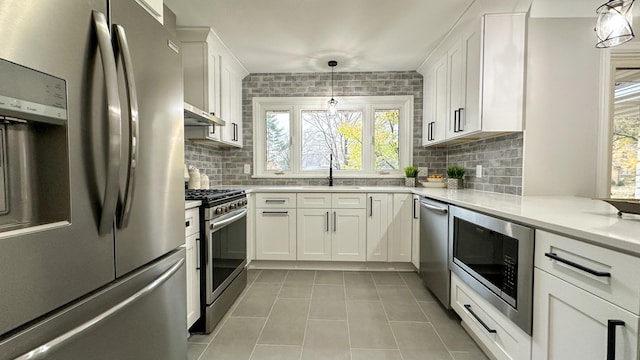 kitchen with tasteful backsplash, white cabinets, hanging light fixtures, and appliances with stainless steel finishes